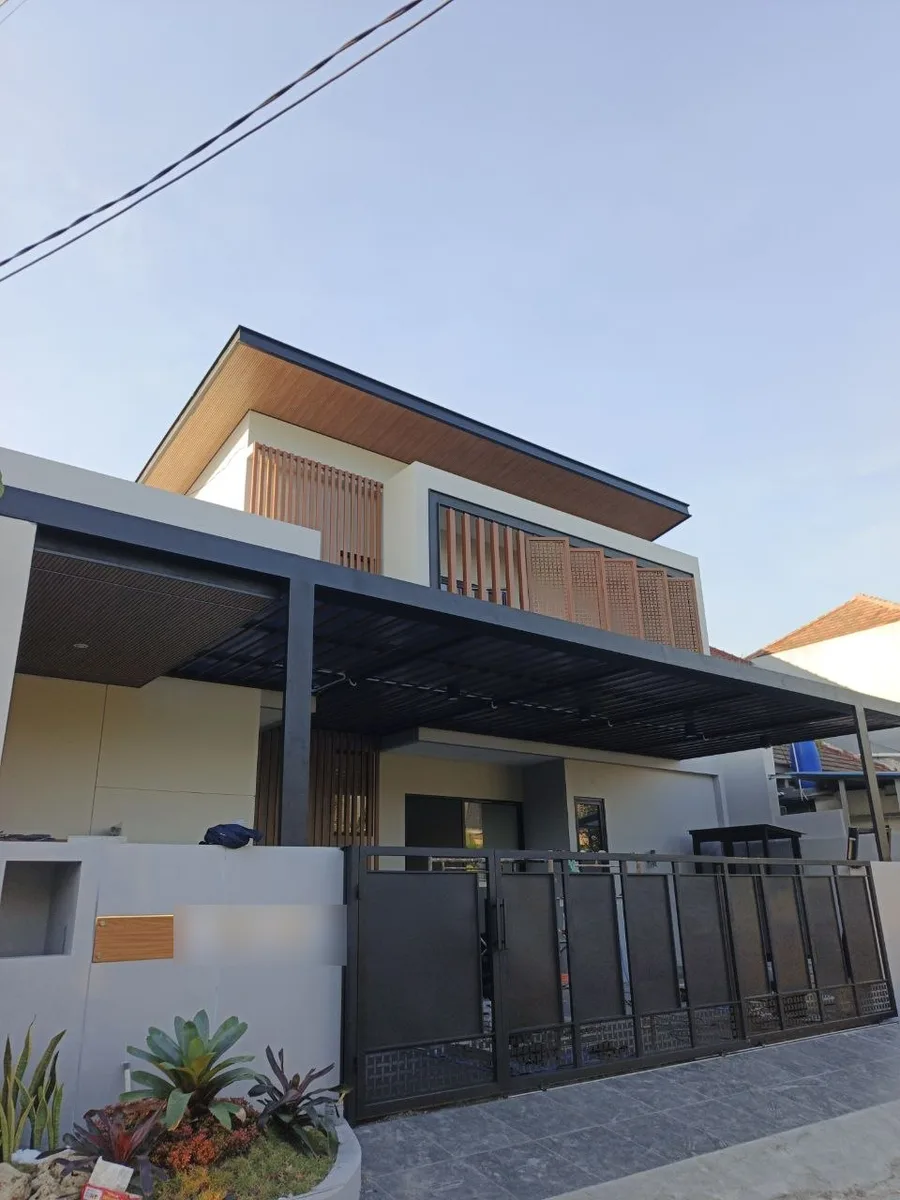 Rumah dua lantai modern tropis dengan kisi kayu di fasad dan kanopi carport baja yang selesai dibangun Madina Build di Perumahan Demangan Residence Lamongan